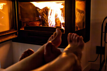 A pair of feet in front of the fireplace. A woman and man warm themselves by the fire.	