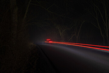 Car riding through forest on road with fog. Long exposure, brake light trail line, transport background