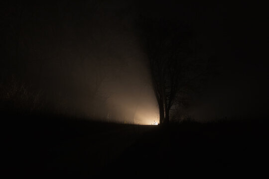 A car driving beyond the horizon on a road with fog creating an illuminated horor silhouette of the landscape. Long exposure, traffic background