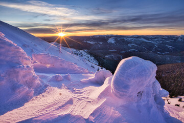 View of the sun's radiant burst over the snow-laden mountain peaks, casting a golden hue on the frosted ground, Nizke Tatry, Zilinsky kraj, Slovakia.