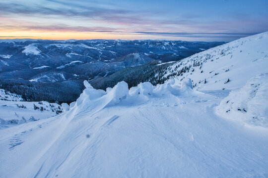 View of a snow-covered mountain slope glistening under the soft hues of dawn, with distant peaks fading into the horizon, Nizke Tatry, Zilinsky kraj, Slovakia.