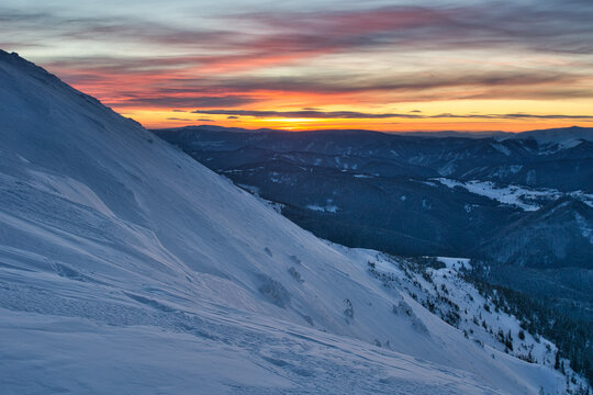 View of snowy mountain slopes under a fiery sunset sky, a serene landscape of winter's embrace, Velka Chochula, Nizke Tatry, Zilinsky kraj, Slovakia.