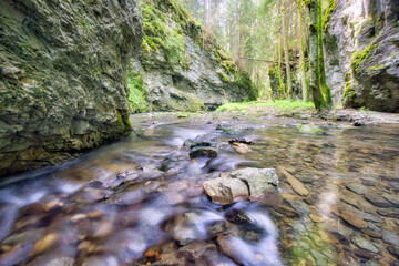 View of a tranquil stream cascading over rocks, framed by moss-covered cliffs and verdant trees, creating a serene natural corridor, Hybicka Tiesnava, Zilinsky kraj, Slovakia.