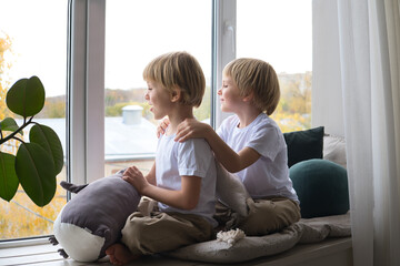 children, blonde twin boys, look out the window, sitting on the window sill