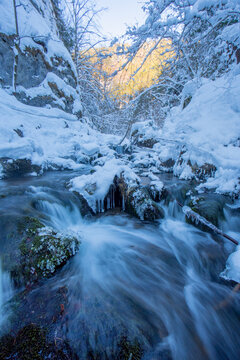 View of a snow-laden stream trickles through an icy gorge, sunlight kissing the distant peaks, a winter wonderland untouched by time, Prosiek, Zilinsky kraj, Slovakia.