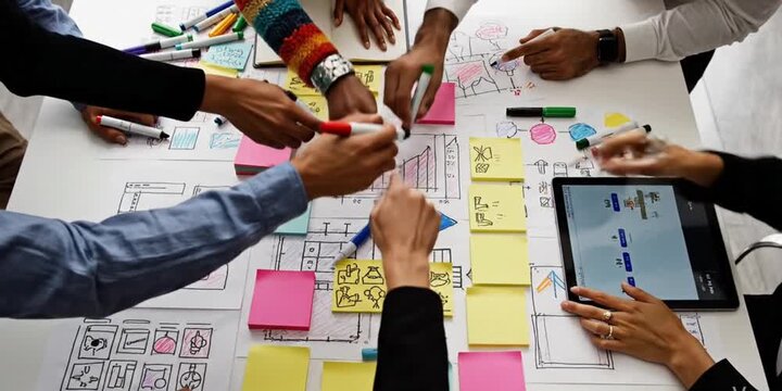 Engaging scene of diverse hands actively participating in a creative brainstorming session for a digital project, showcasing vibrant markers and sketches on a tabletop. SACTR