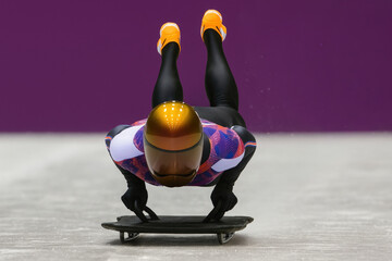 Skeleton athlete gliding down track with legs raised. Concept of streamlined technique, winter racing discipline, athlete form analysis and high-speed sport visuals for editorial applications.