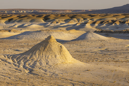 View of sun-soaked arid landscape with undulating sandy hills and textured rock formations under a clear sky, Senek, Mangystau Region, Kazakhstan.