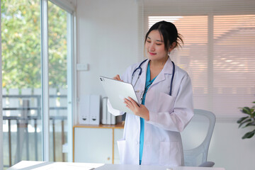 Young Asian doctor in a white coat and scrubs using a digital tablet for patient records in a modern medical office