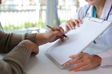 Patient hand holding pen, signing a medical consent form on a clipboard with a doctor in a healthcare consultation
