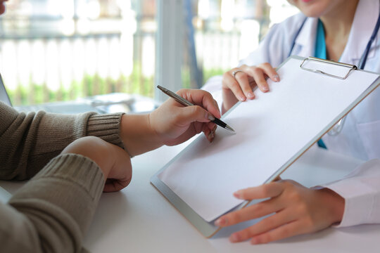 Patient hand holding pen, signing a medical consent form on a clipboard with a doctor in a healthcare consultation