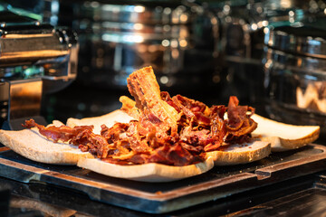 Heap of Crispy Fried Bacon Strips on Toasted Bread in Hotel Kitchen