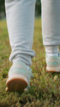 closeup sneakers walking on green grass, slow steady stride across park meadow, casual sweatpants and mint trainers, focus on sole pattern and foot motion, peaceful morning mood and mindful pace
