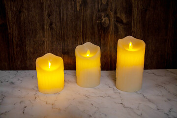 Festive three yellow candles on a dark brown board background. Holiday, Christmas, New Year, postcards.