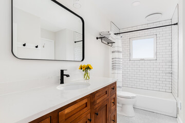A bright and clean modern bathroom featuring a wooden vanity with a white countertop, black fixtures, and a subway tile shower.