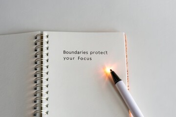 Notebook with a pen and the message 'Boundaries protect your Focus' glowing from a light source