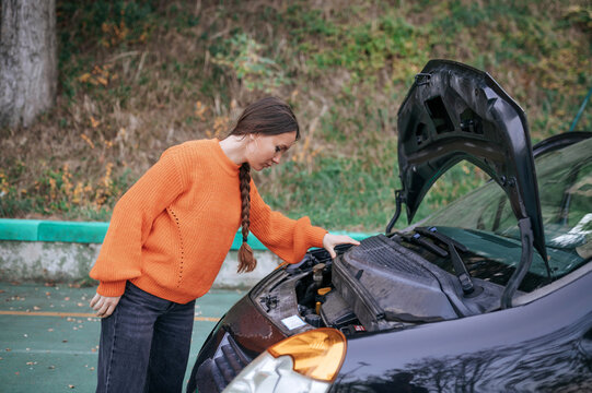 Woman checking engine of a parked car outdoors