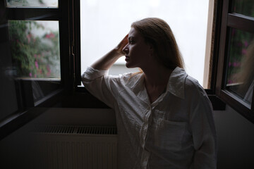 Woman in thoughtful silhouette by window in low light