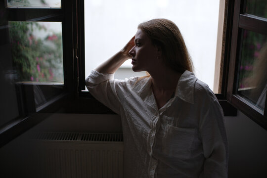 Woman in thoughtful silhouette by window in low light