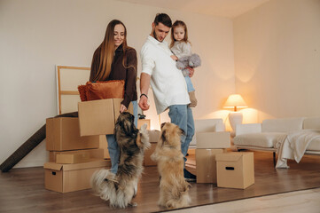 Fototapeta premium Conception of new life. Happy young family with child and dog moving into new home, standing among cardboard boxes