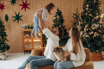 Sitting, relaxing together. Happy family with child and dog celebrating Christmas at home with decorated tree