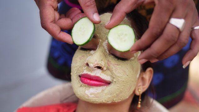 A woman with facial mask and fresh cucumber on eyes relaxing at home. Close-up portrait of smiling girl in clay mask. homemade multani mitti face pack treatment, skin care, beauty.