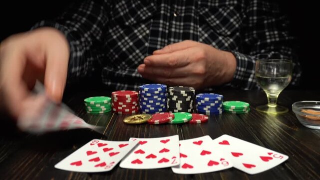 A player sits at a wooden table, laying out his winning cards straight flush. Nearby are numerous poker chips and a glass of drink, as the gambling continues late into the night.
