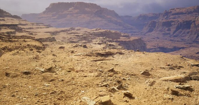 Vast arid terrain stretches endlessly, showcasing jagged rock formations and the subtle interplay of light and shadows. A dramatic backdrop of towering cliffs complements the barren expanse.