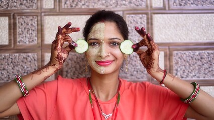 Spa woman with facial mask and fresh cucumber on eyes, relaxing at home. Close-up portrait of...