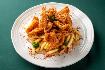 Crispy fried chicken tenders served with golden french fries and a creamy sauce on a white plate, close-up, elevated view