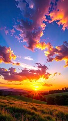 Vivid sunset paints sky, illuminating landscape, grass, & fields. Rays of sun