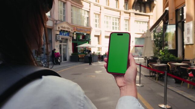 A female tourist walks through the city streets with a backpack, holding her phone with a green screen. Using travel apps. High quality 4k footage