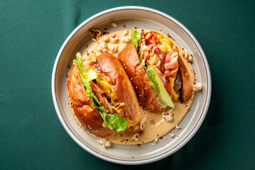 A close-up shot of several mini burgers, or sliders, served in a bowl with rich cheese sauce,...