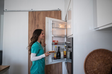 Female nurse picking up sandwich from refrigerator in kitchen