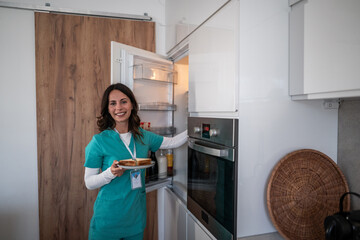 Female healthcare worker smiling having sandwich at home kitchen