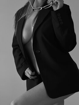 A girl in a jacket on a naked body with glasses in her hands, her face is not visible. Boudoir photo shoot of a girl