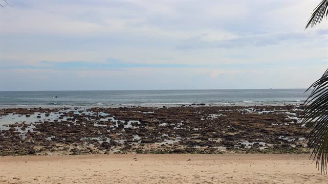 Rocky coastal landscape exposed at low tide. Irregular rock formations stretch toward the calm, blue sea under an overcast sky.