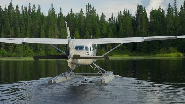 Seaplane driving across open lake water with forest shoreline in quiet quebec wilderness, rearview slow motion, Seignurie Du Triton Quebec Canada