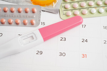Pregnancy test with birth control pills and condom for female on calendar, ovulation day.