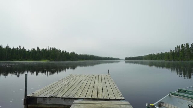 A wooden dock extending into a calm misty lake surrounded by forest, Quebec, Canada