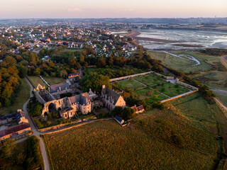 Obraz premium Aerial view of Abbaye de Beauport at Paimpol, bathed in golden hour light, with tidal flats and coastal scenery stretching into the background.