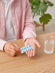 Person holding blue pills in hand near a glass of water on wooden table