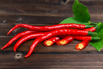 Fresh red chili peppers with green stems lying on a wooden plank background