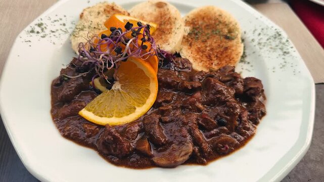 Wild boar stewed in red wine with spices, served with dumplings and garnished with an orange slice and sprouts. High quality 4k footage