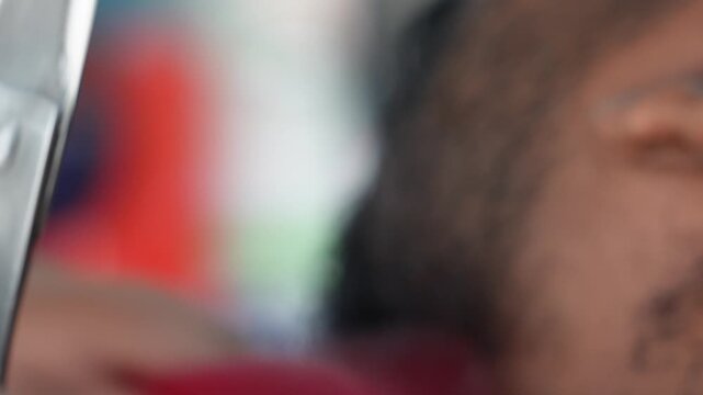 A barber hands are using a red comb and scissors to trim beard