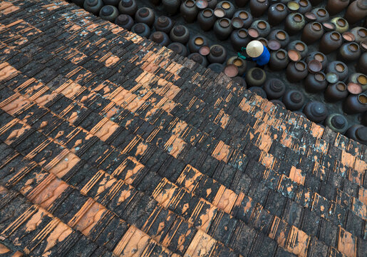 Aerial view of contrasting textures and tones as terracotta tiles meet rows of earthen pots under the watchful eye of a lone worker, Hung Yen, Hung Yen, Vietnam.