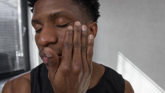 Close-up view of African American young man softly rubbing face cream into skin to keep it hydrated and healthy