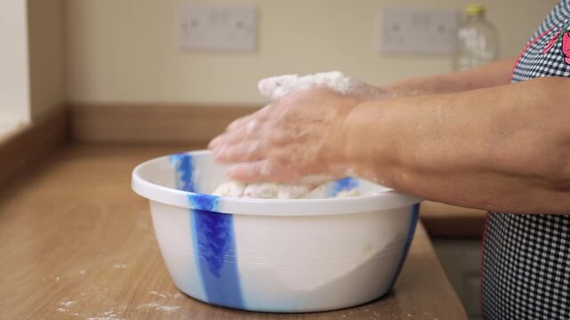 Kneading dough in bowl with hands. Unrecognizable person shaping mixture in container. Working flour and ingredients into mass. Preparing dough for homemade bread