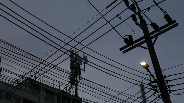 Dense tangle of utility wires and cables forming a busy silhouette around a wooden pole against a deep blue evening sky, urban electric infrastructure complexity.