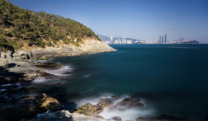 View of rocky coastline meets the deep blue sea, contrasting with a distant skyline under a clear sky, Busan, Busan, South Korea.